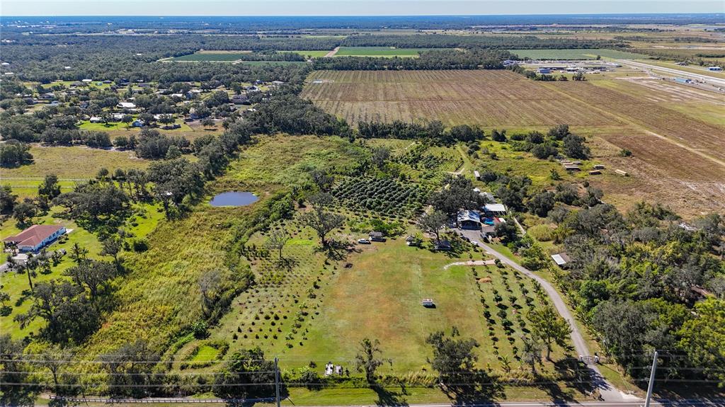 An aerial view shows a rural property with a house, outbuildings, trees, and a pond — 21552 E STATE ROAD 64, BRADENTON, FL