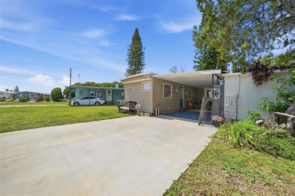 A tan mobile home with a carport and concrete driveway sits on a grassy lot — 6439 TOWER DRIVE, HUDSON, FL