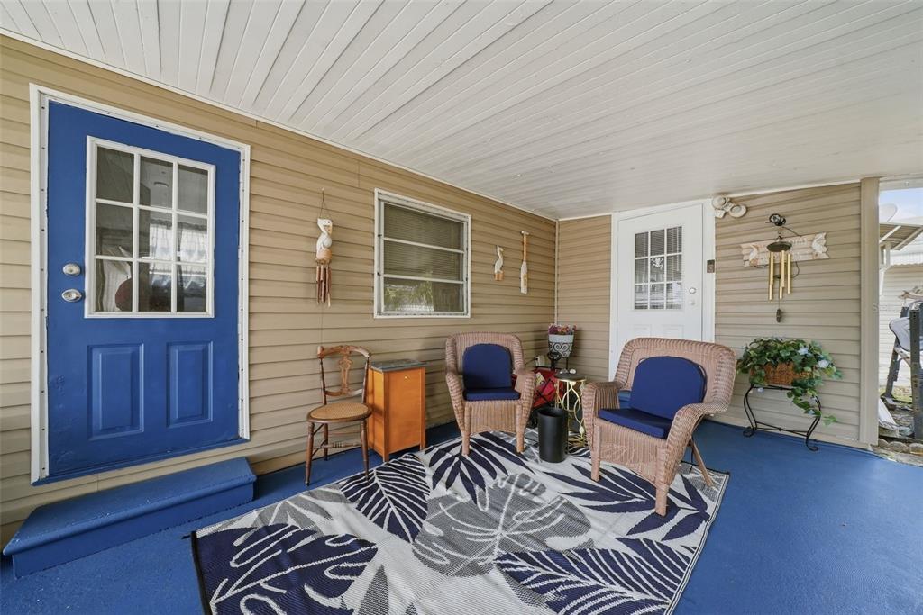 A covered porch with tan siding, a blue door, wicker chairs, and a patterned area rug — 6439 TOWER DRIVE, HUDSON, FL
