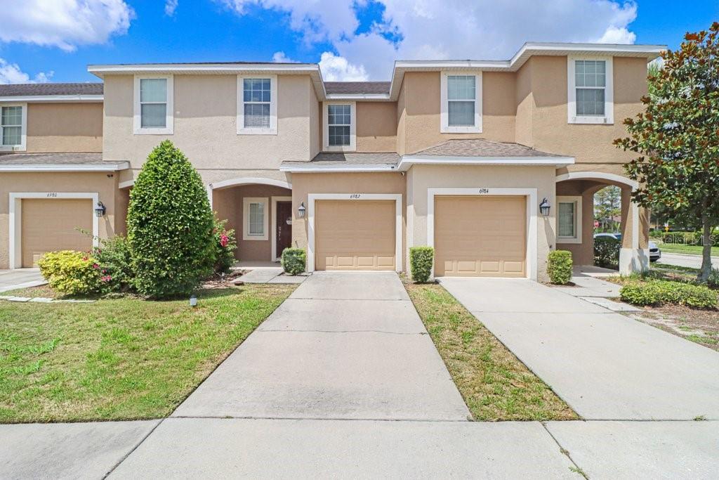 A row of two-story townhomes with beige stucco exteriors, tan garage doors, and concrete driveways — 6982 HOLLY HEATH DRIVE, RIVERVIEW, FL