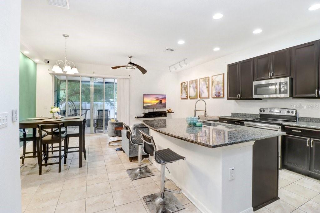 An open-concept kitchen and living area featuring dark cabinets, granite countertops, and tile flooring — 6982 HOLLY HEATH DRIVE, RIVERVIEW, FL