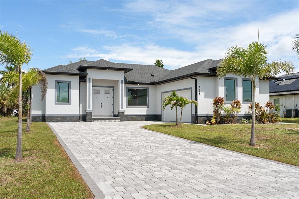 A modern single-story house with a white stucco facade, dark trim, and a paved driveway — 9487 ROSEBUD CIRCLE, PORT CHARLOTTE, FL
