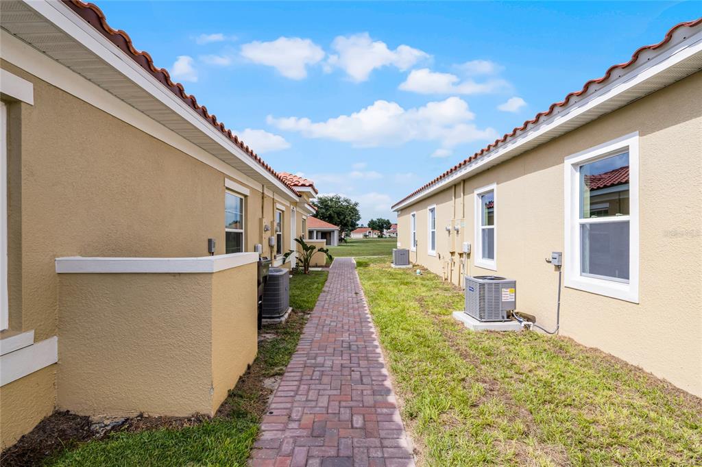 A brick walkway runs between the exterior walls of two tan stucco residential buildings — 1826 CORIANDER DRIVE, KISSIMMEE, FL