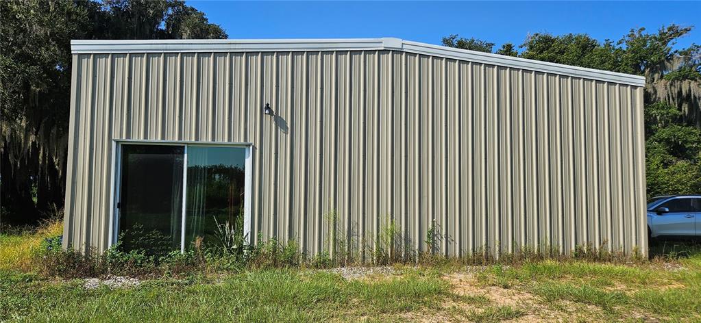 A beige metal-sided building features a sliding glass door and an exterior light fixture — 691 S LAKE PATRICK ROAD, FROSTPROOF, FL