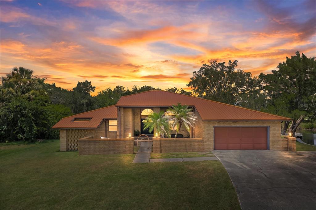A brick house with a metal roof and a gated courtyard at sunset — 11649 W CLUBVIEW DRIVE, HOMOSASSA, FL