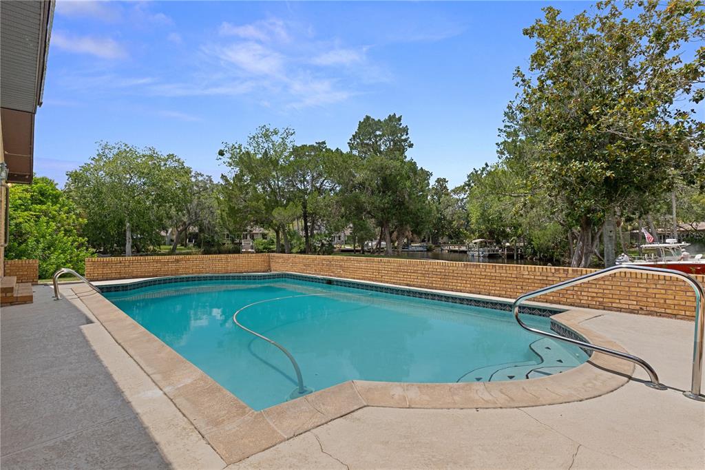 An outdoor swimming pool with a brick wall enclosure overlooks a canal with docked boats — 11649 W CLUBVIEW DRIVE, HOMOSASSA, FL