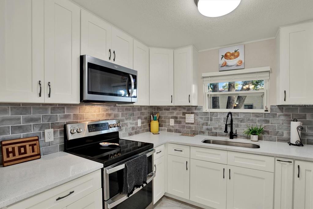 A kitchen features white cabinets, a stainless steel microwave, a black stove, and gray backsplash — 1945 OVERBROOK AVENUE, CLEARWATER, FL
