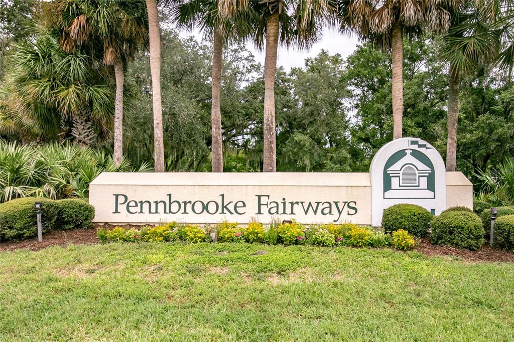 A beige monument sign for Pennbrooke Fairways stands in front of palm trees and landscaping — 639 NE COTTAGE PARK LANE, LEESBURG, FL