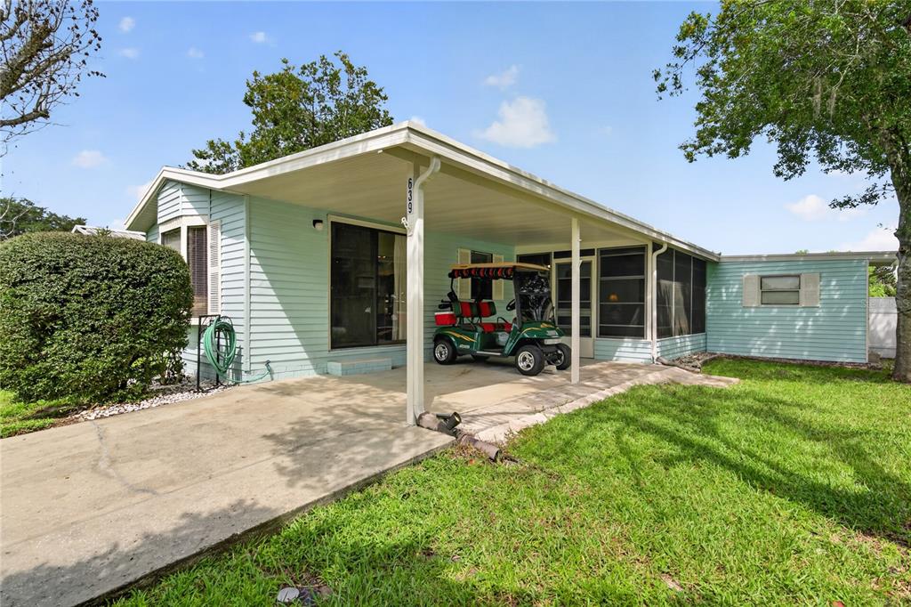A light blue mobile home features a concrete driveway, a covered carport, and a golf cart — 639 NE COTTAGE PARK LANE, LEESBURG, FL