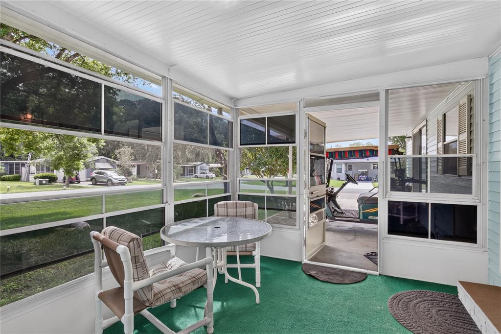 A screened-in porch features a round glass table, two chairs, and green carpeting — 639 NE COTTAGE PARK LANE, LEESBURG, FL