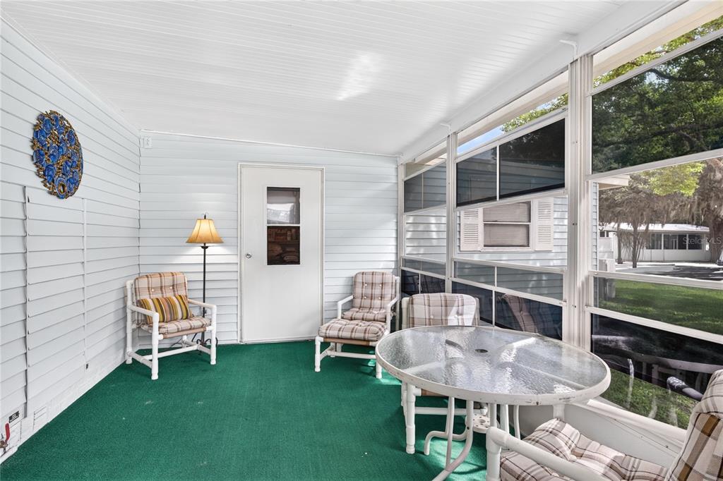 A sunroom features white paneled walls, a green carpet, a glass table, and several chairs — 639 NE COTTAGE PARK LANE, LEESBURG, FL