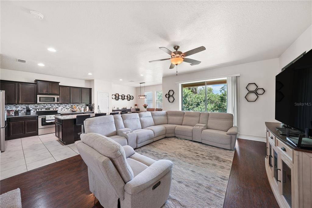 A living room with a large sectional sofa, dark wood floors, and an open kitchen — 8415 LOBLOLLY PINE COURT, RIVERVIEW, FL