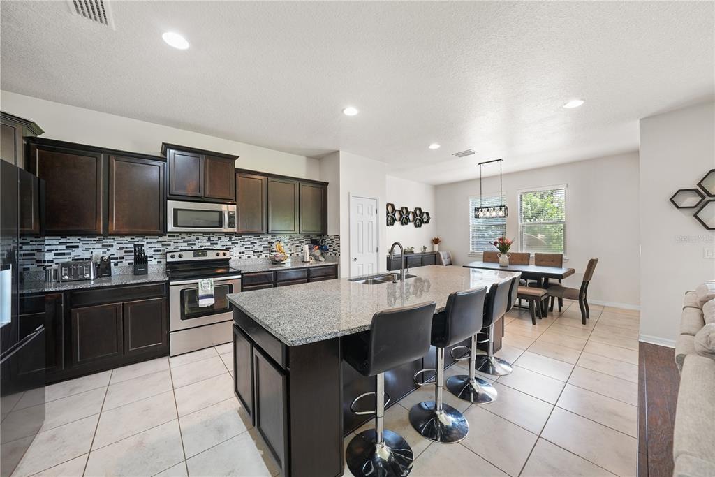 A kitchen with dark wood cabinets, granite countertops, a center island, and an adjacent dining area — 8415 LOBLOLLY PINE COURT, RIVERVIEW, FL