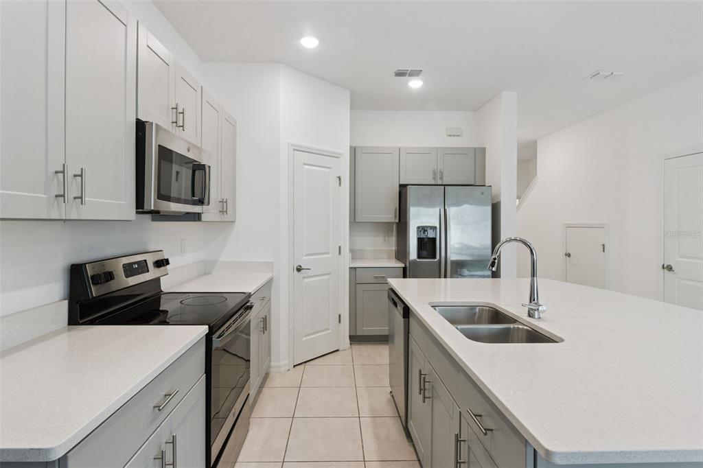 A modern kitchen features gray cabinets, white countertops, stainless steel appliances, and a central island — 2251 PORTRAIT STREET, POINCIANA, FL