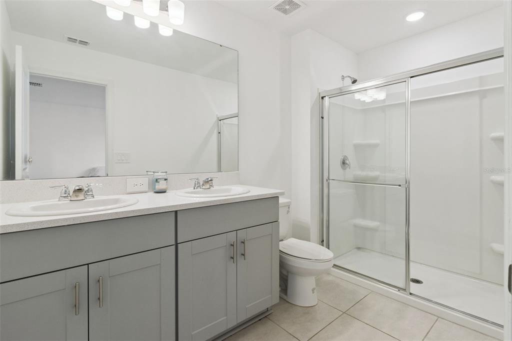 A bathroom features a double-sink vanity with gray cabinets, a toilet, and a glass-enclosed shower — 2251 PORTRAIT STREET, POINCIANA, FL