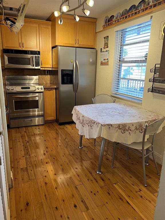 A kitchen features light wood cabinets, stainless steel appliances, a dining table, and hardwood floors — 3910 INVERRARY BOULEVARD UNIT B301, LAUDERHILL, FL