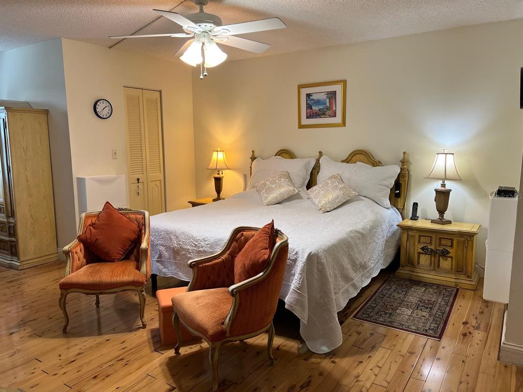 A bedroom features a king bed, two orange armchairs, wooden flooring, and a ceiling fan — 3910 INVERRARY BOULEVARD UNIT B301, LAUDERHILL, FL