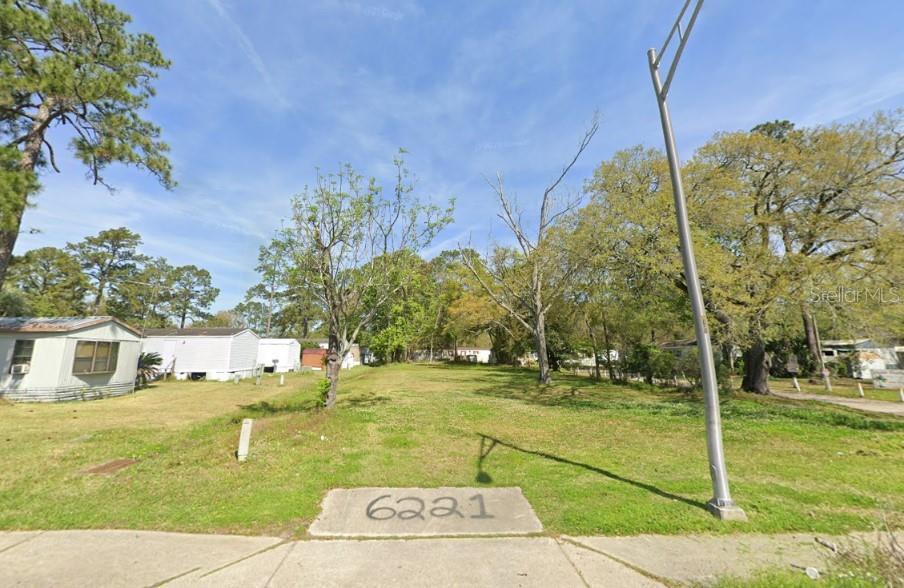 A vacant grassy lot sits between two mobile homes under a clear blue sky — 6221 COLLINS ROAD, JACKSONVILLE, FL