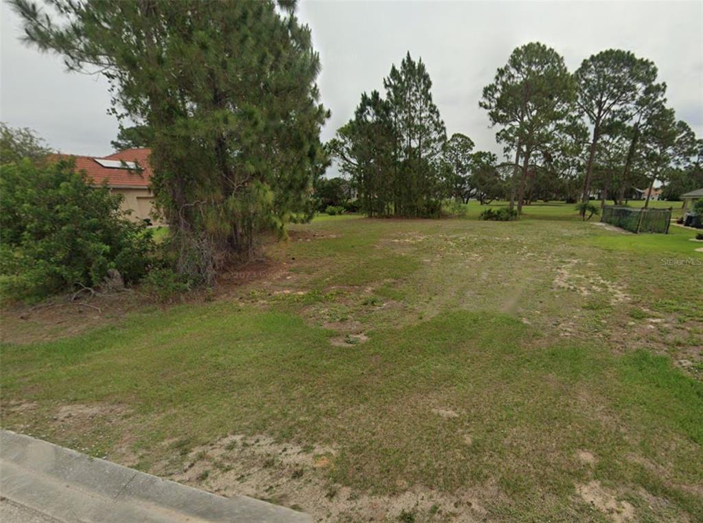 A vacant, grassy residential lot is bordered by trees and neighboring houses — 5016 MAGNOLIA PLACE, SEBRING, FL
