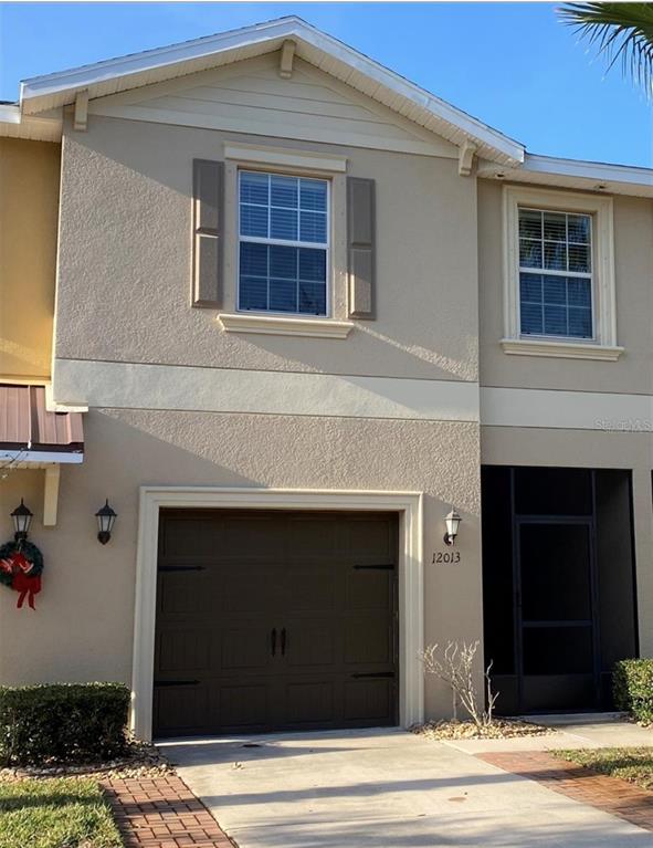 A two-story townhouse exterior features a single-car garage, a screened entryway, and beige stucco siding — 12013 GREENGATE DRIVE, HUDSON, FL