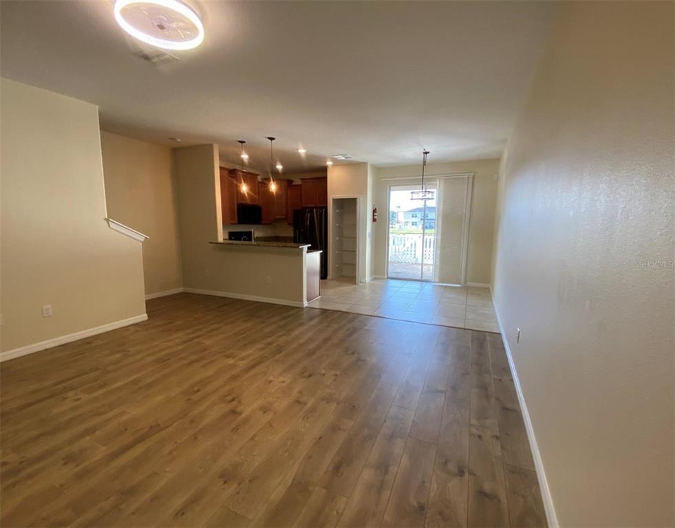 An open-concept living area features wood-look flooring, a kitchen with dark cabinets, and sliding doors — 12013 GREENGATE DRIVE, HUDSON, FL