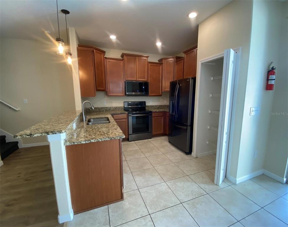 A kitchen features wood cabinets, granite countertops, stainless steel appliances, and tile flooring — 12013 GREENGATE DRIVE, HUDSON, FL