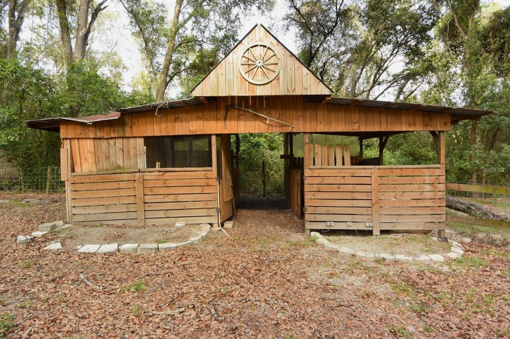 A rustic wooden barn with a wagon wheel decoration sits in a wooded outdoor area — 17438 LAWLESS ROAD, SPRING HILL, FL