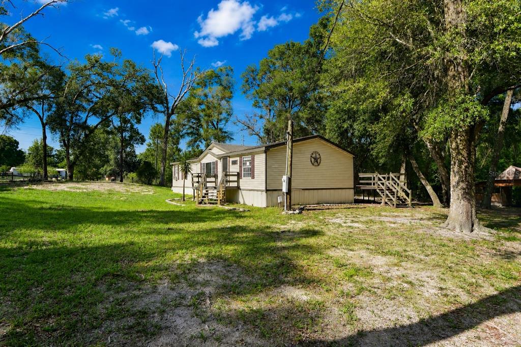 A single-story manufactured home sits on a grassy lot surrounded by mature trees — 17438 LAWLESS ROAD, SPRING HILL, FL