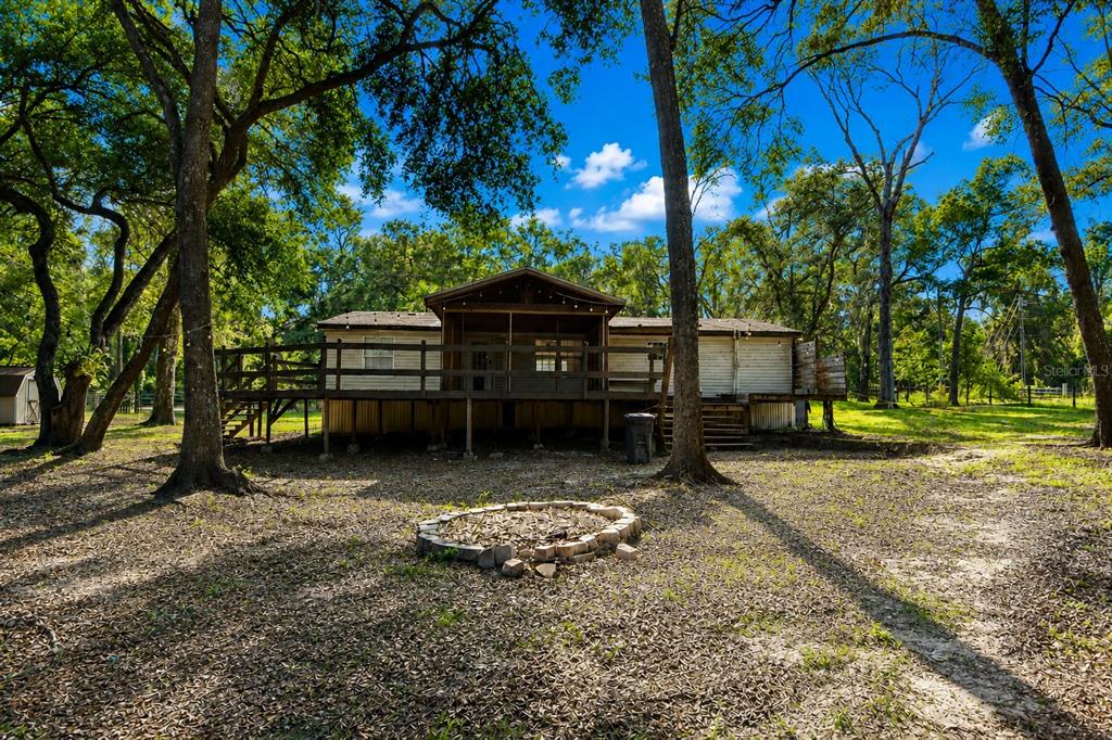 A single-story house with a large wooden deck and a stone fire pit in front — 17438 LAWLESS ROAD, SPRING HILL, FL