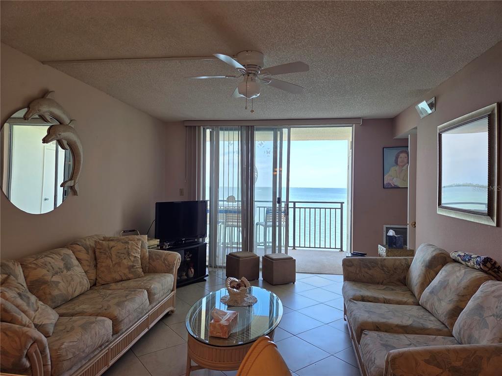 A living room features two floral sofas, a glass coffee table, and a balcony view — 9 HAIG PLACE UNIT 405, DUNEDIN, FL