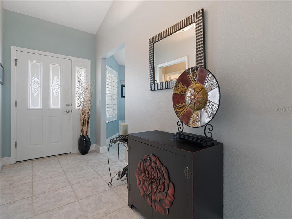 A foyer features tile flooring, a dark cabinet with a floral design, and a wall mirror — 490 LITTLE RIVER PATH, THE VILLAGES, FL