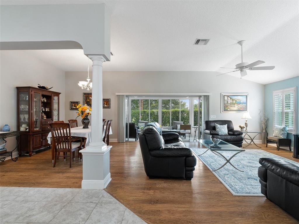 A living and dining room with wood floors, a white column, and sliding glass doors — 490 LITTLE RIVER PATH, THE VILLAGES, FL