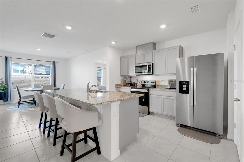 A kitchen features a granite-topped island, light gray cabinetry, stainless steel appliances, and tile flooring — 11400 AMBER RIDGE DRIVE, ZELLWOOD, FL