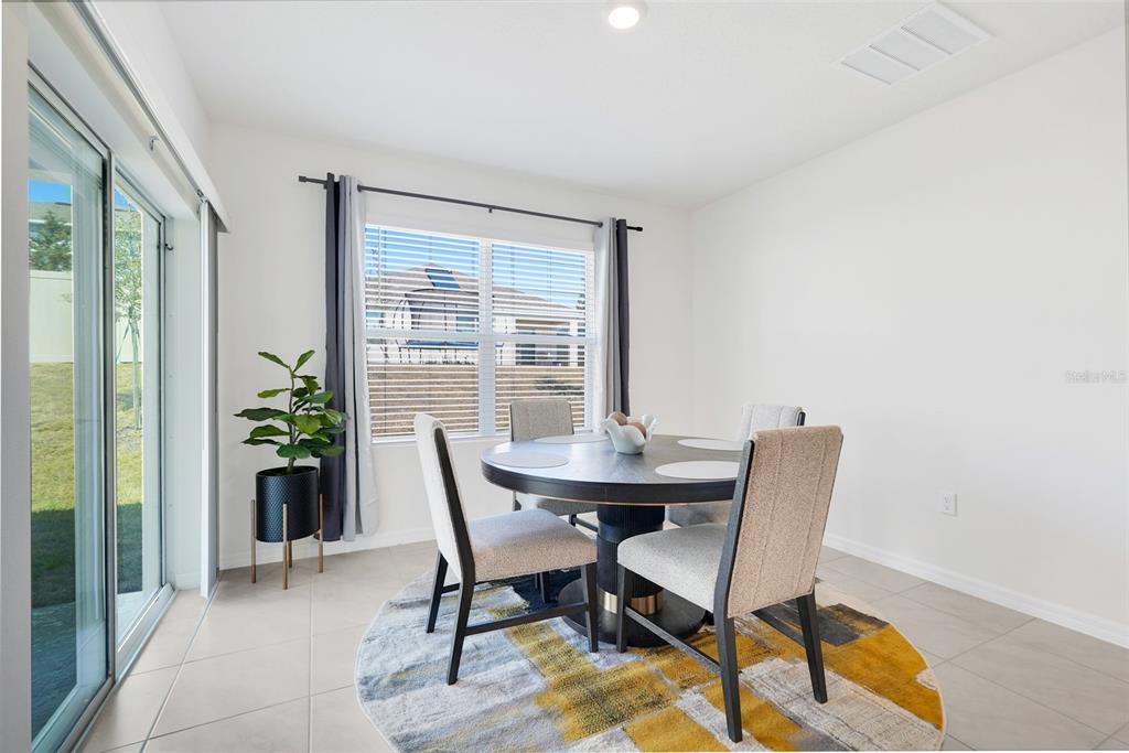 A dining area features a round table, four chairs, a patterned rug, and sliding glass doors — 11400 AMBER RIDGE DRIVE, ZELLWOOD, FL