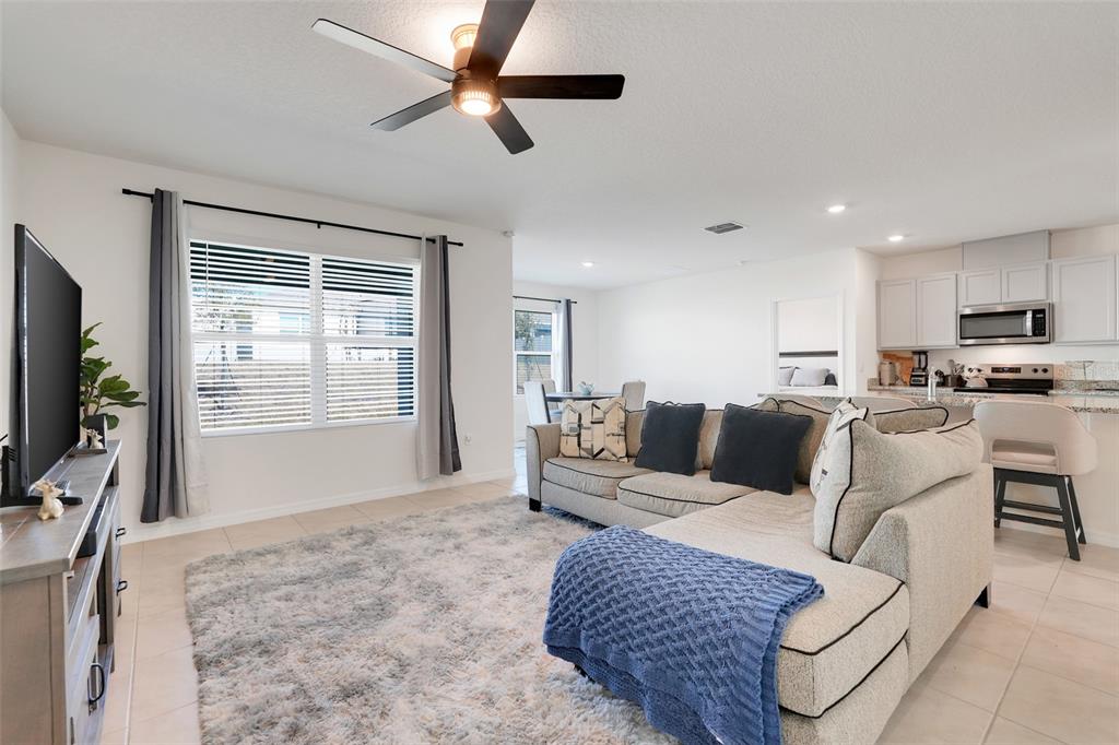 A living room with a sectional sofa, area rug, ceiling fan, and open kitchen — 11400 AMBER RIDGE DRIVE, ZELLWOOD, FL