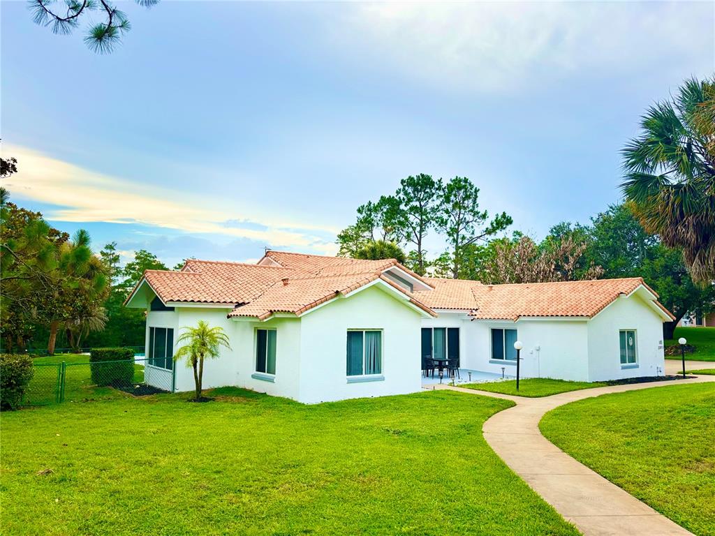 A white single-story house with a terracotta tile roof sits on a grassy lawn — 12853 BELLERIVE DRIVE, CLERMONT, FL