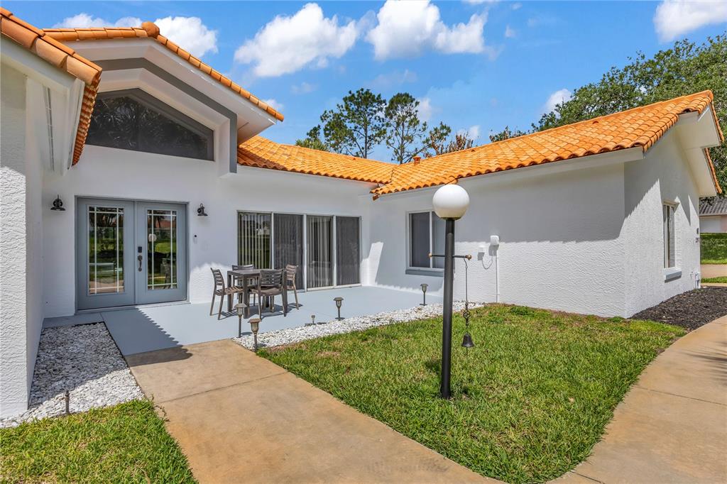 A white house with an orange tile roof features a patio and a grassy yard — 12853 BELLERIVE DRIVE, CLERMONT, FL