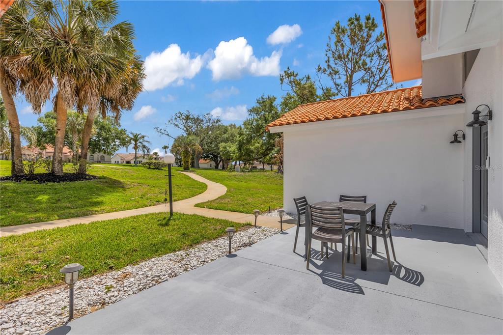 A patio with a dining set sits beside a house with a tiled roof — 12853 BELLERIVE DRIVE, CLERMONT, FL