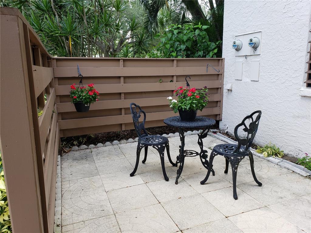 A small patio features a bistro set, two chairs, and hanging flower baskets against a fence — 138 PINENEEDLE DRIVE, BRADENTON, FL