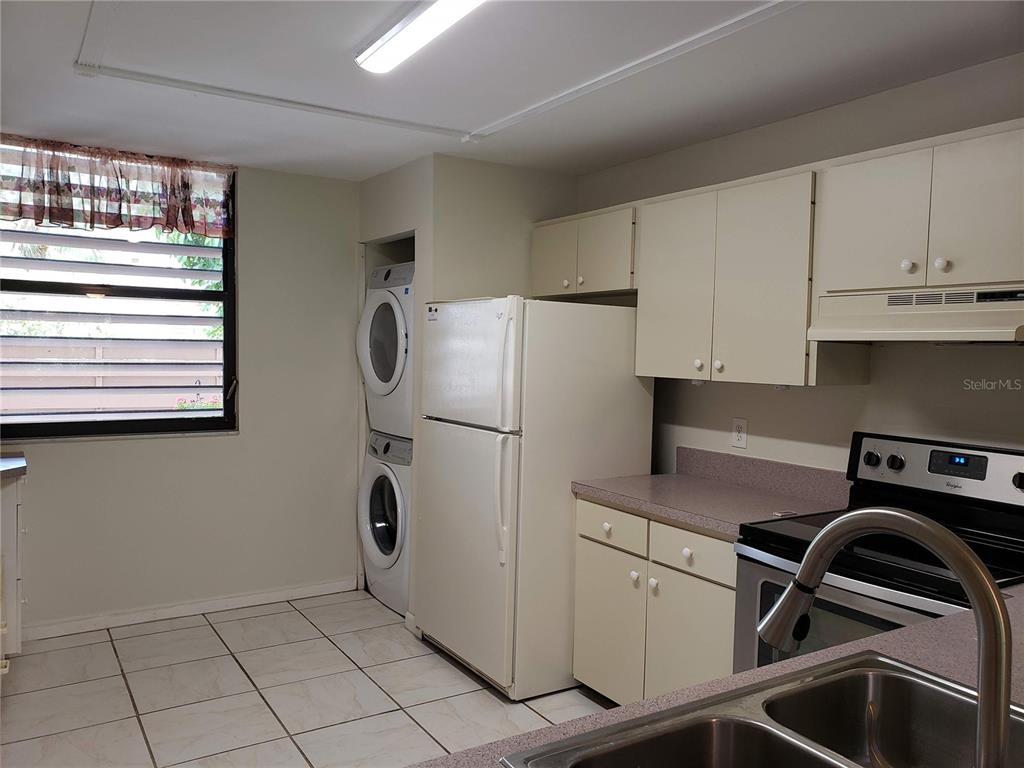 A kitchen features white cabinets, a refrigerator, a stacked washer-dryer unit, and tiled flooring — 138 PINENEEDLE DRIVE, BRADENTON, FL