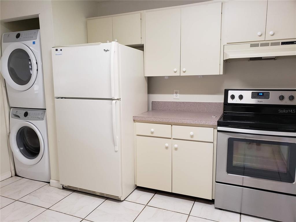 A kitchen features white cabinets, a refrigerator, a stacked washer and dryer, and a stove — 138 PINENEEDLE DRIVE, BRADENTON, FL