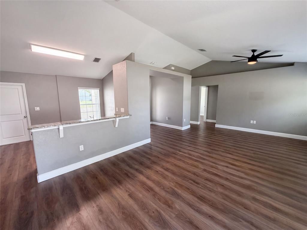 An open-concept living area features gray walls, wood-look flooring, a vaulted ceiling, and a kitchen island — 11413 SAND HILL AVENUE, SPRING HILL, FL