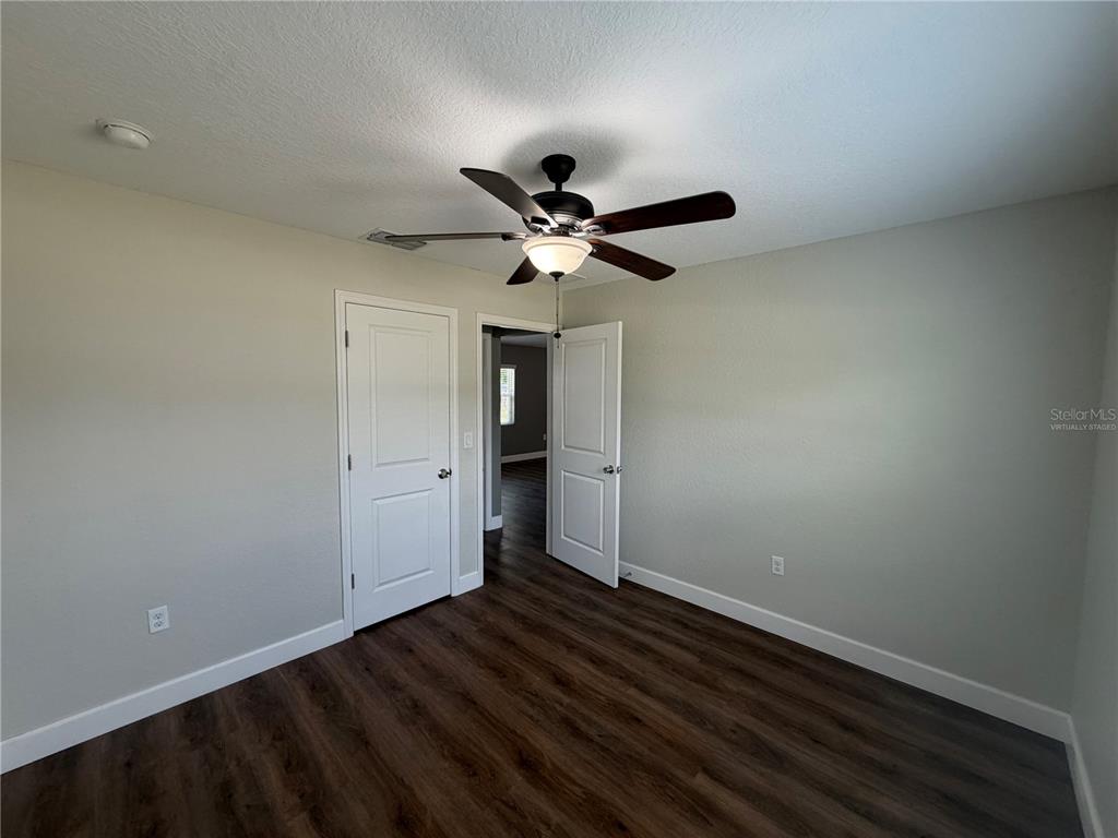 A bedroom features wood-look flooring, a ceiling fan, and two white interior doors — 11413 SAND HILL AVENUE, SPRING HILL, FL