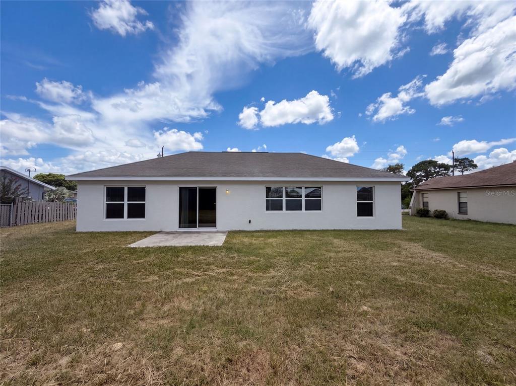 The rear exterior of a white, single-story house features a sliding glass door and windows — 11413 SAND HILL AVENUE, SPRING HILL, FL
