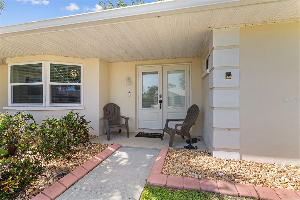A concrete walkway leads to a covered front porch with two chairs and double doors — 5776 AUGUSTA CIRCLE, SARASOTA, FL