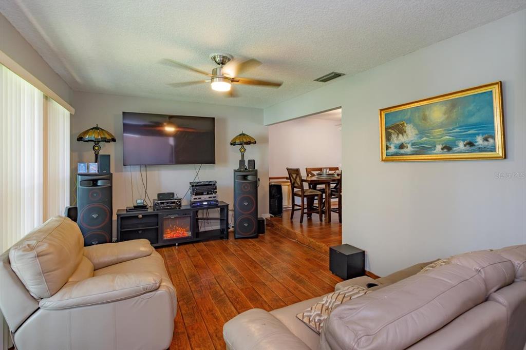 A living room with wood flooring, a television, and a dining area in the background — 211 STEVENAGE DRIVE, LONGWOOD, FL