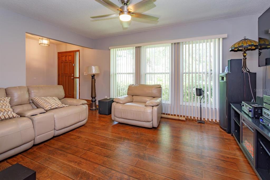 A living room features light-colored leather furniture, wood-look flooring, and large vertical blinds — 211 STEVENAGE DRIVE, LONGWOOD, FL