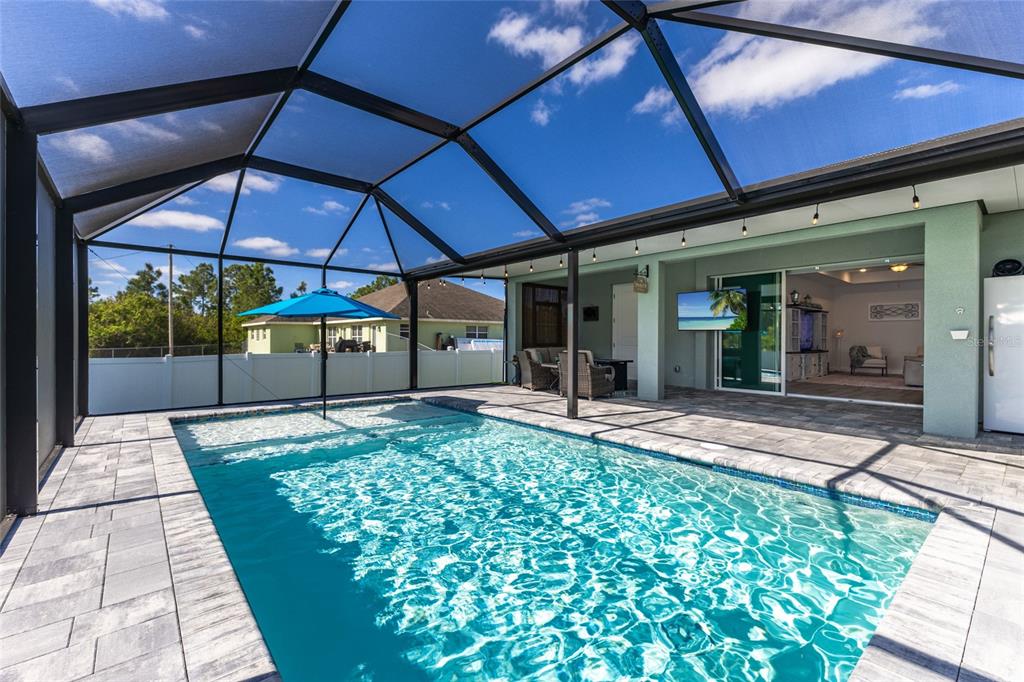 A single-story house exterior at night features a two-car garage and a screened front porch — 908 HIBISCUS AVENUE, LEHIGH ACRES, FL