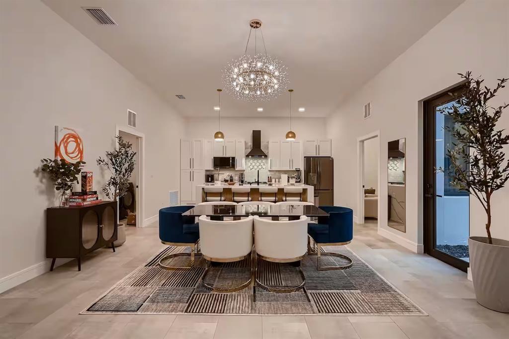 A dining area with a modern chandelier, a glass table, and chairs opens to a kitchen — 13509 PARK BOULEVARD, SEMINOLE, FL