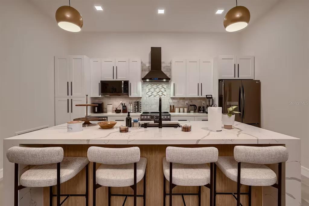 A modern kitchen features white cabinetry, a large quartz island, and four upholstered bar stools — 13509 PARK BOULEVARD, SEMINOLE, FL